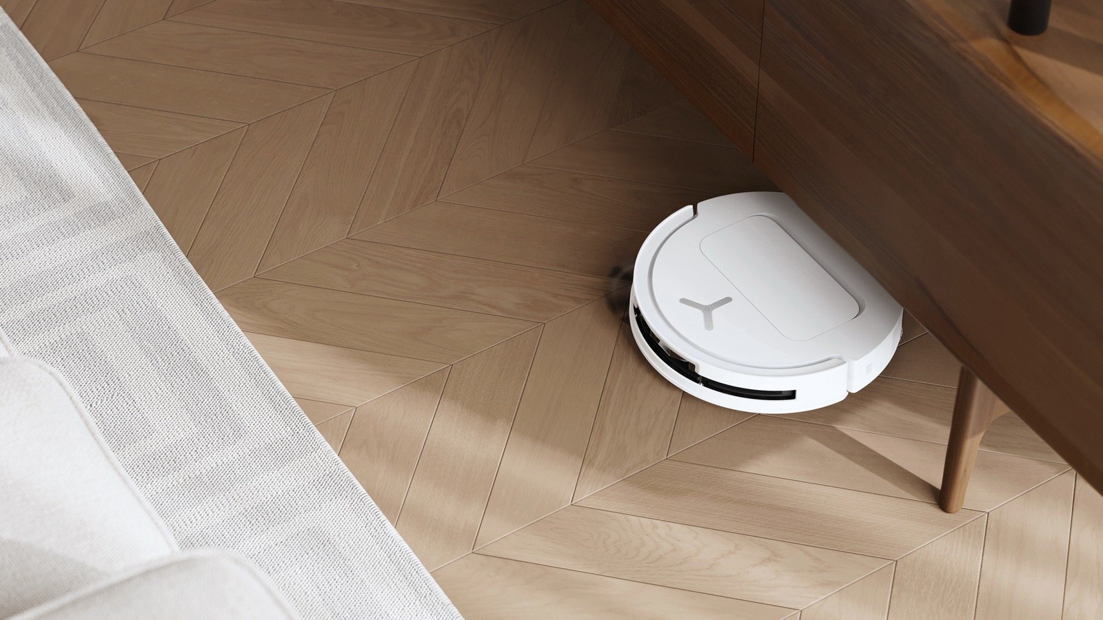 White robot vacuum cleaning herringbone wood flooring as it passes under a wooden table